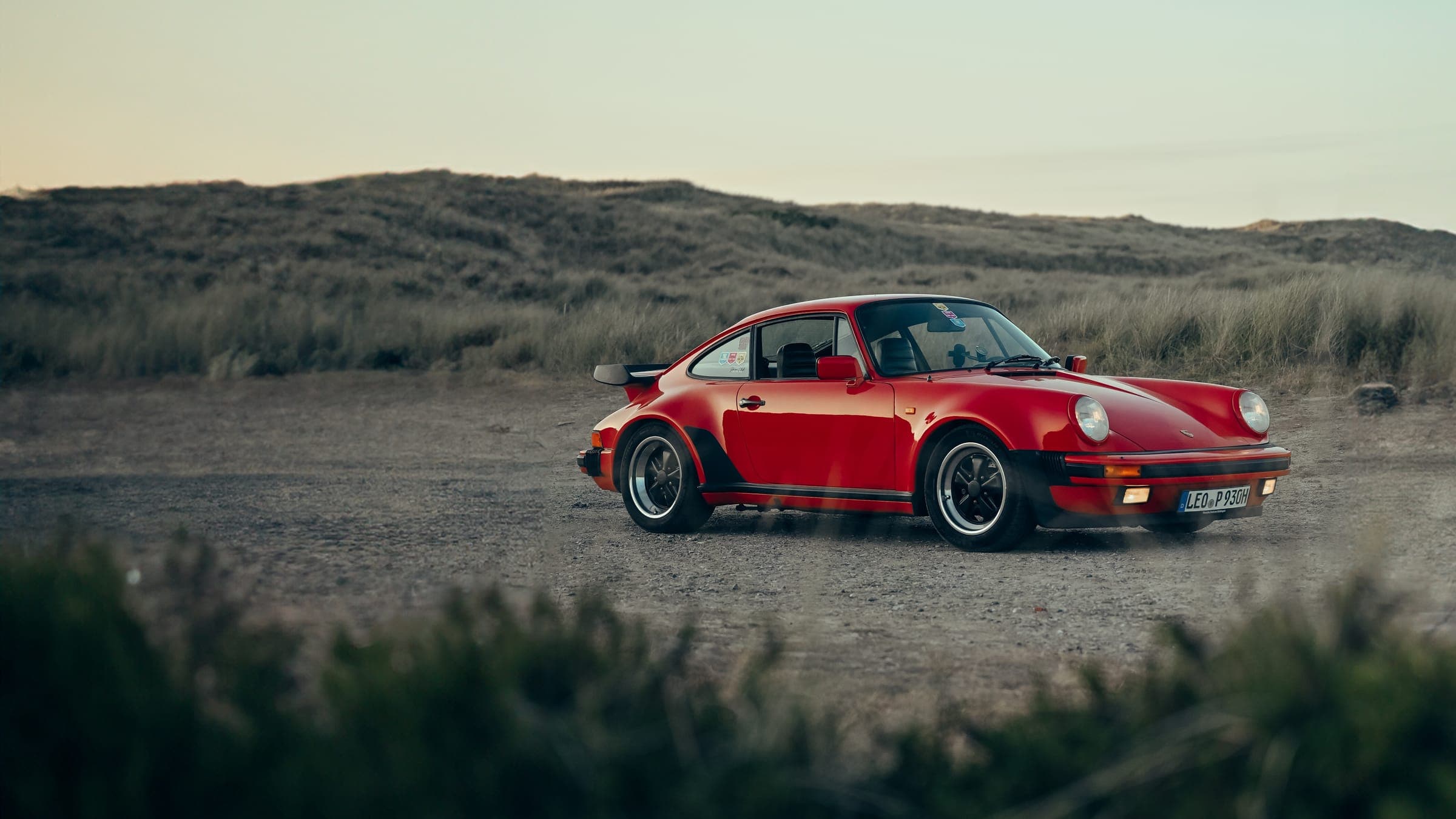 Roter Porsche 911 Turbo der Baureihe 930 auf einem Schotterweg in den Dünen
